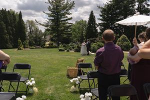 Wedding guests seated outdoors watch a bride and groom approach during a garden ceremony on a sunny day.