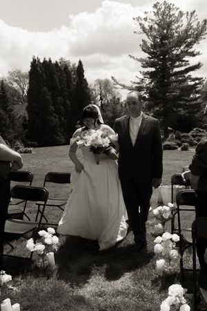 Black and white photo of bride and escort walking down outdoor aisle.