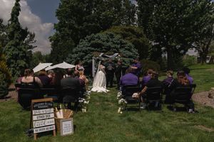Wide shot of an intimate outdoor wedding ceremony on a green lawn with guests seated in black chairs.
