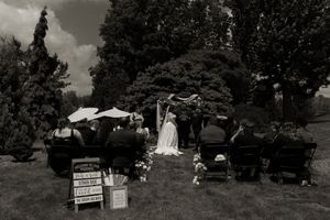Black and white photo of outdoor wedding ceremony with seated guests and decorative signs on lawn.