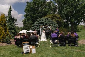 Small intimate outdoor wedding ceremony with guests seated on lawn facing couple at floral altar.