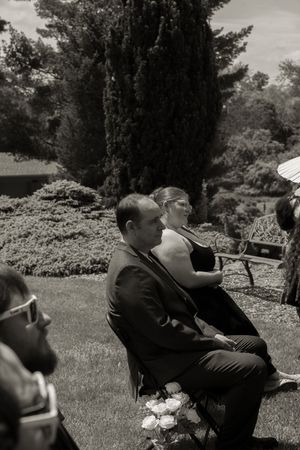 Black and white photo of wedding guests seated outdoors on lawn during garden ceremony.