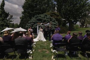 Outdoor wedding ceremony with bride and groom at altar, guests seated in chairs on lush green lawn.