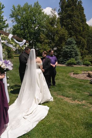 Outdoor wedding ceremony with bride in cathedral veil and groom at altar in garden setting.