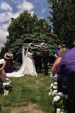 A bride and groom exchange vows at an outdoor wedding altar decorated with white flowers and draped fabric.
