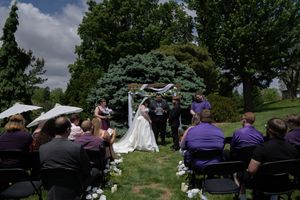 Outdoor wedding ceremony with guests seated in purple attire under sunny sky.