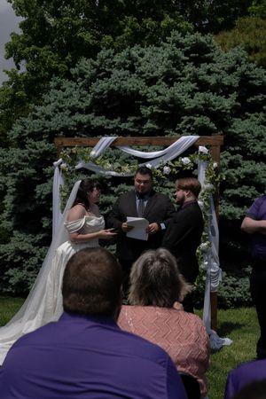 Bride and groom exchange vows under floral arch with officiant at outdoor garden wedding ceremony.