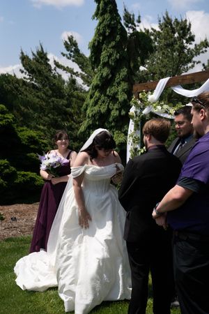 Bride in white gown and groom exchange rings at outdoor wedding ceremony under decorated arch.