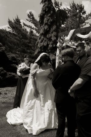 Black and white photo of bride and groom during outdoor wedding ceremony under floral arch.