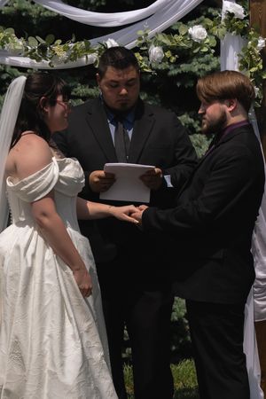 Officiant reads vows as bride and groom hold hands at decorated outdoor altar.