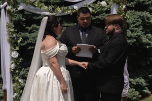 Bride and groom hold hands during vow exchange with officiant at outdoor ceremony.