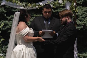 Bride and groom exchanging vows at outdoor wedding altar decorated with white draping and flowers.