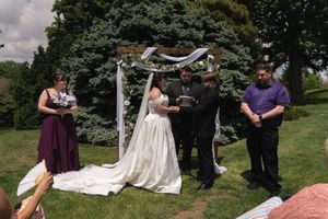 Bride and groom hold hands during outdoor wedding ceremony under white draped floral arch.