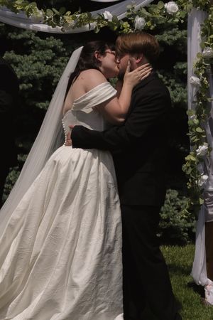 Bride and groom share first kiss at outdoor wedding ceremony under floral arch with white dress and veil.