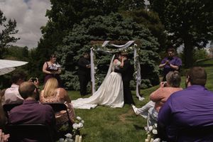 Bride and groom share a kiss under a floral arch at an outdoor garden wedding ceremony.