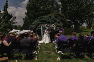 Wide shot of outdoor wedding ceremony with guests in purple seated in garden aisle.