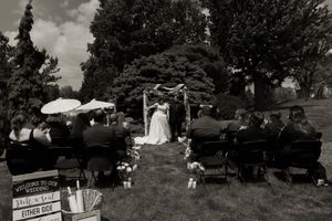 Black and white wide shot of outdoor wedding ceremony with seated guests on lawn.