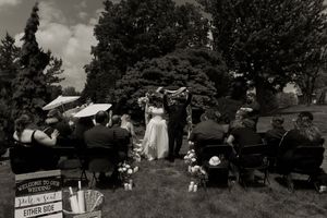 Black and white wide shot of outdoor wedding ceremony with seated guests and decorated altar.