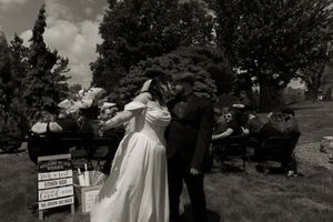 Black and white photo of newlyweds sharing first kiss at outdoor garden wedding ceremony with guests seated behind.