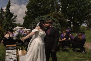 Bride and groom sharing a kiss outdoors at garden wedding ceremony with guests seated nearby.