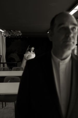 Black and white photo of bride in veil and groom in dark suit at indoor venue.