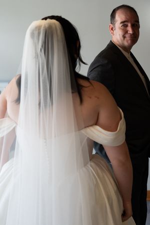 Bride in white gown and veil shares first look moment with smiling man in dark suit.