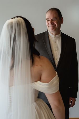 Groom smiling at bride in white off-shoulder wedding dress and veil during emotional first look moment.