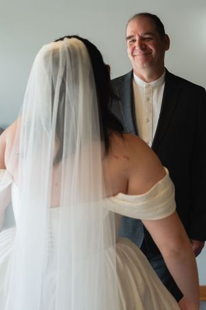 Groom smiles warmly at bride wearing white off-shoulder wedding gown and veil during their first look moment.