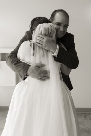 Black and white photo of a smiling man in a suit embracing a bride in a white wedding gown.