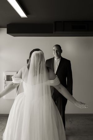 Black and white photo of a bride in a white gown and veil facing a smiling man in a black suit.