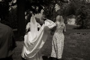 Black and white photo of bride in white gown and veil walking with bridesmaid through garden.