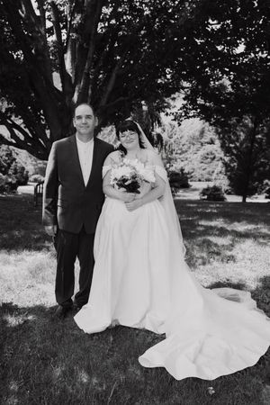 Black and white portrait of a bride and groom smiling together under a large tree after their wedding.