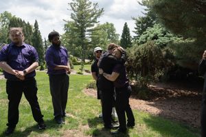 Wedding guests in formal attire embrace and socialize outdoors in a lush green garden setting.