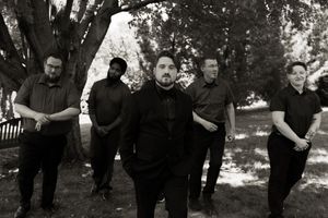 Black and white group portrait of five formally dressed people standing under large tree.