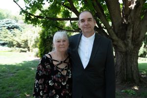 Mature couple poses together under a tree at an outdoor wedding celebration.