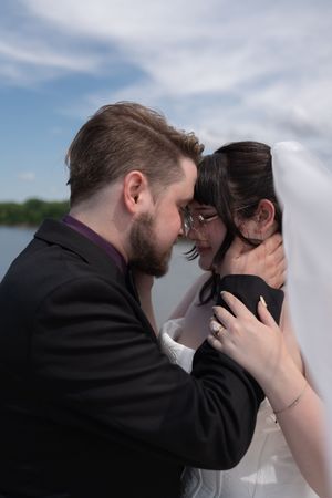 Bride and groom share an intimate forehead-to-forehead moment under wedding veil by waterfront.