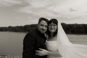 Black and white wedding portrait of bride and groom embracing near a scenic waterfront location.