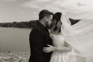 Black and white photo of bride and groom sharing an intimate moment by the river, veil blowing.