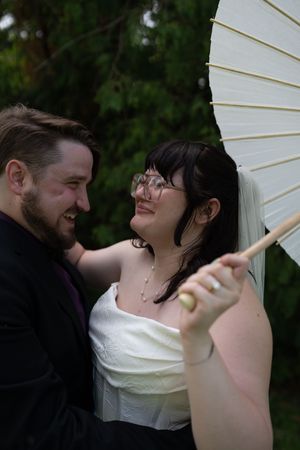 Smiling bride and groom share a romantic moment under a white parasol umbrella outdoors.