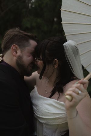 A bride and groom share an intimate moment under a white parasol at their outdoor wedding ceremony.