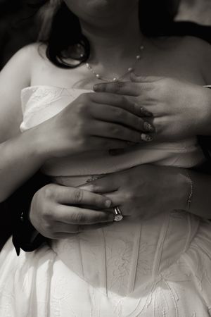 Black and white close-up of bride and groom holding hands showing wedding and engagement rings.