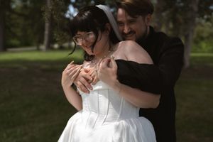 Groom in black suit embracing bride in white corset dress outdoors.