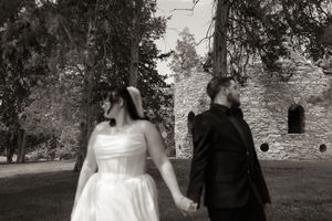 Black and white photo of bride and groom holding hands walking near historic stone ruins.