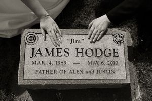 Two hands rest on gravestone of James Hodge, father of Alex and Justin, in touching wedding day memorial tribute.