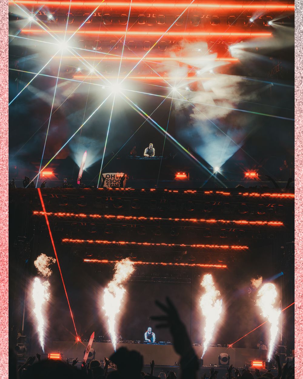 DJ performs on pyramid stage with dramatic laser lights and fire pyrotechnics at packed concert venue.