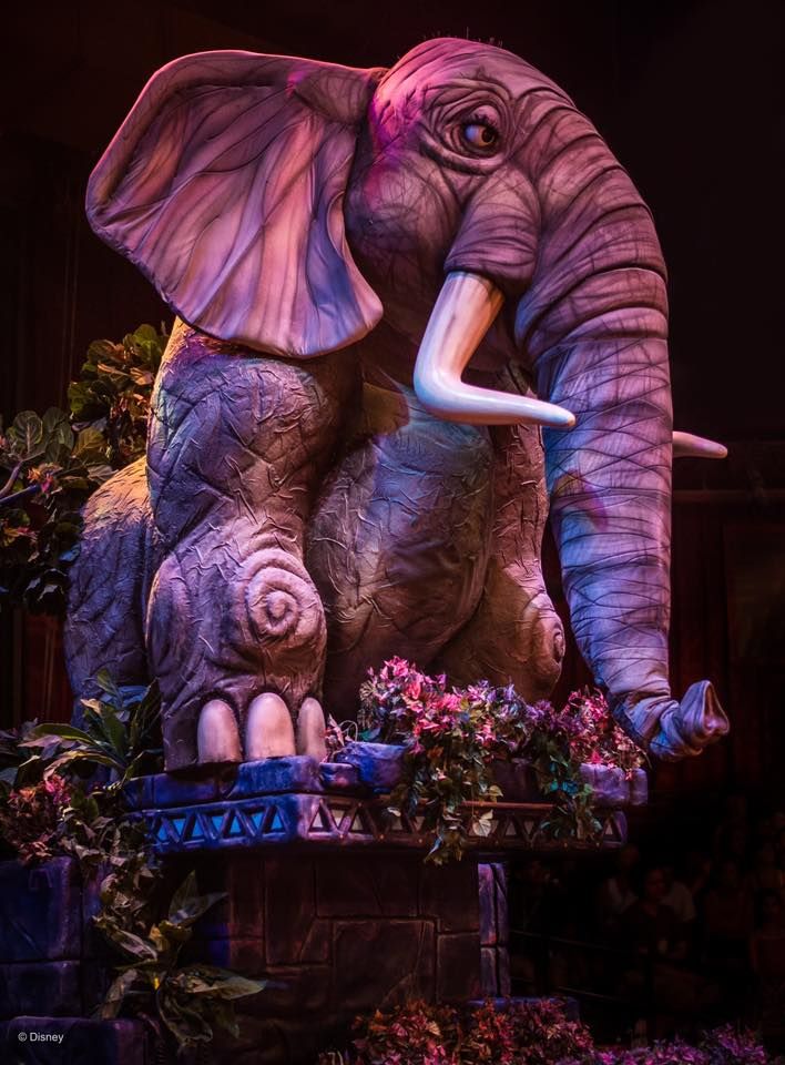 Illuminated purple animatronic elephant puppet with detailed wrinkles and tusks in a Disney theme park attraction.