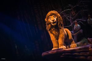 Majestic animatronic lion figure perched on a rock with dramatic lighting in a Disney theatrical show.