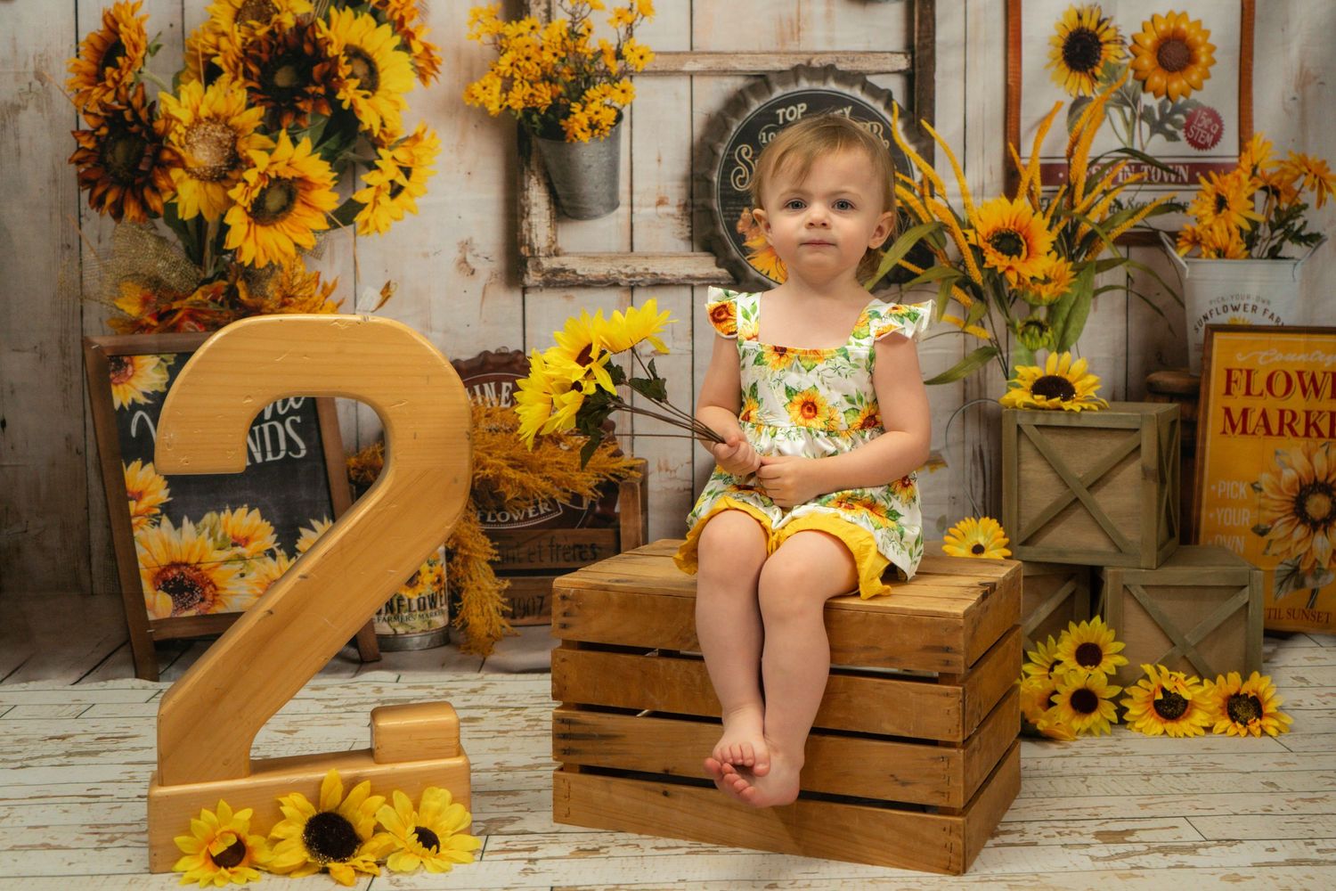 A festive birthday setup with wooden number 2, sunflowers, and wooden crates creating a warm autumn themed photography scene.