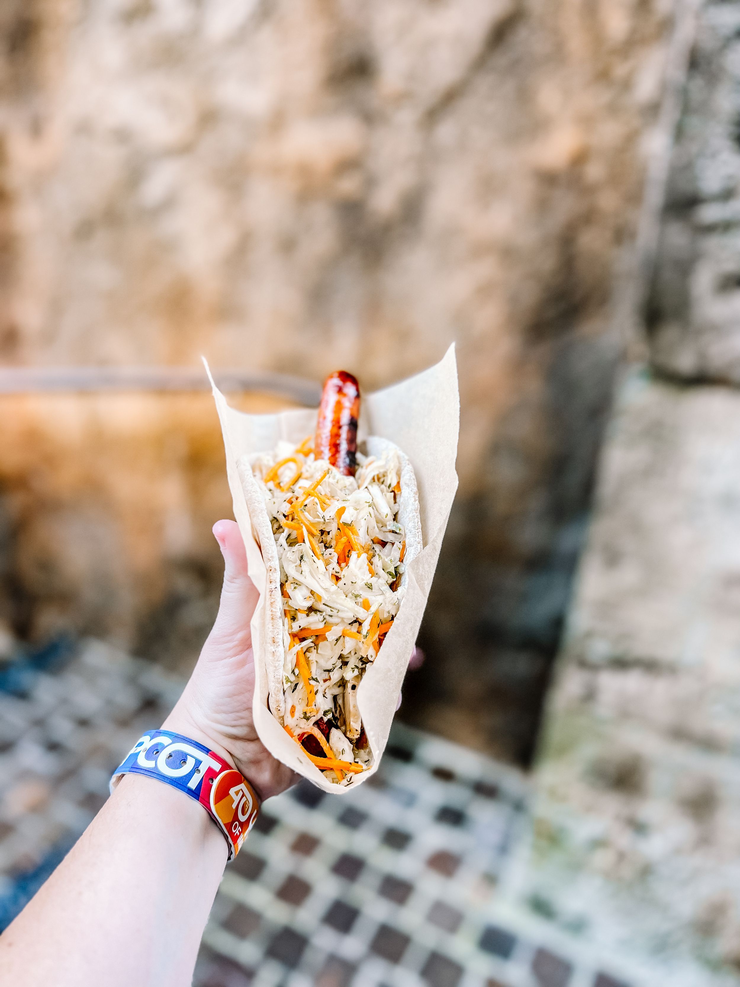 Close-up of a ronto wrap sandwich held against a stone wall background.