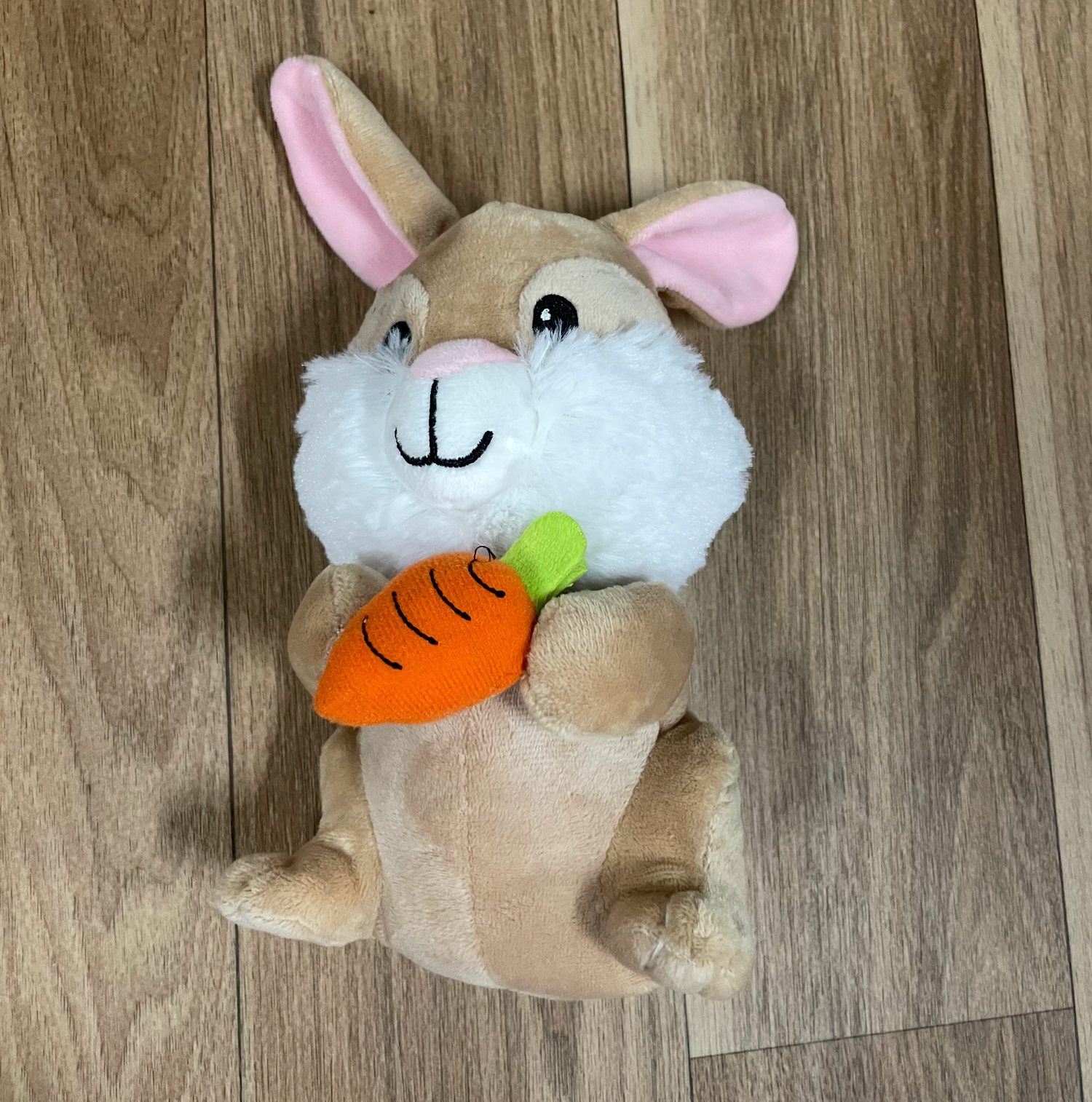 Stuffed rabbit toys with pink ears and orange carrots arranged on hardwood floor.